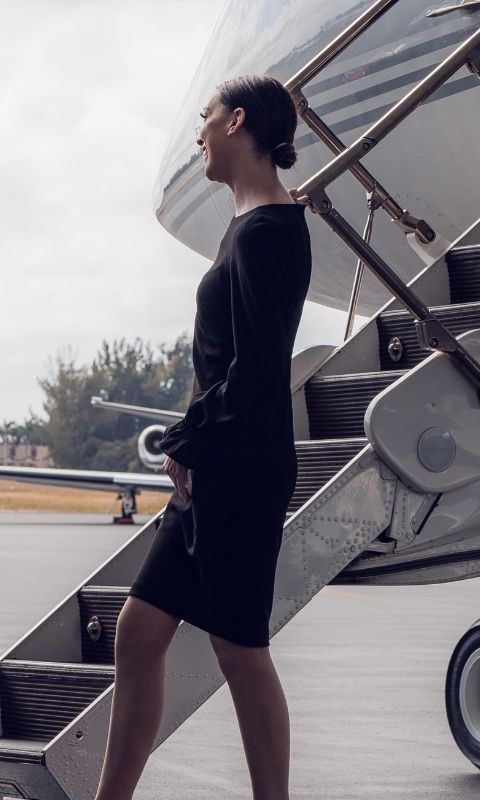 a member of the cabin crew waiting by the steps of a plane to greet passengers